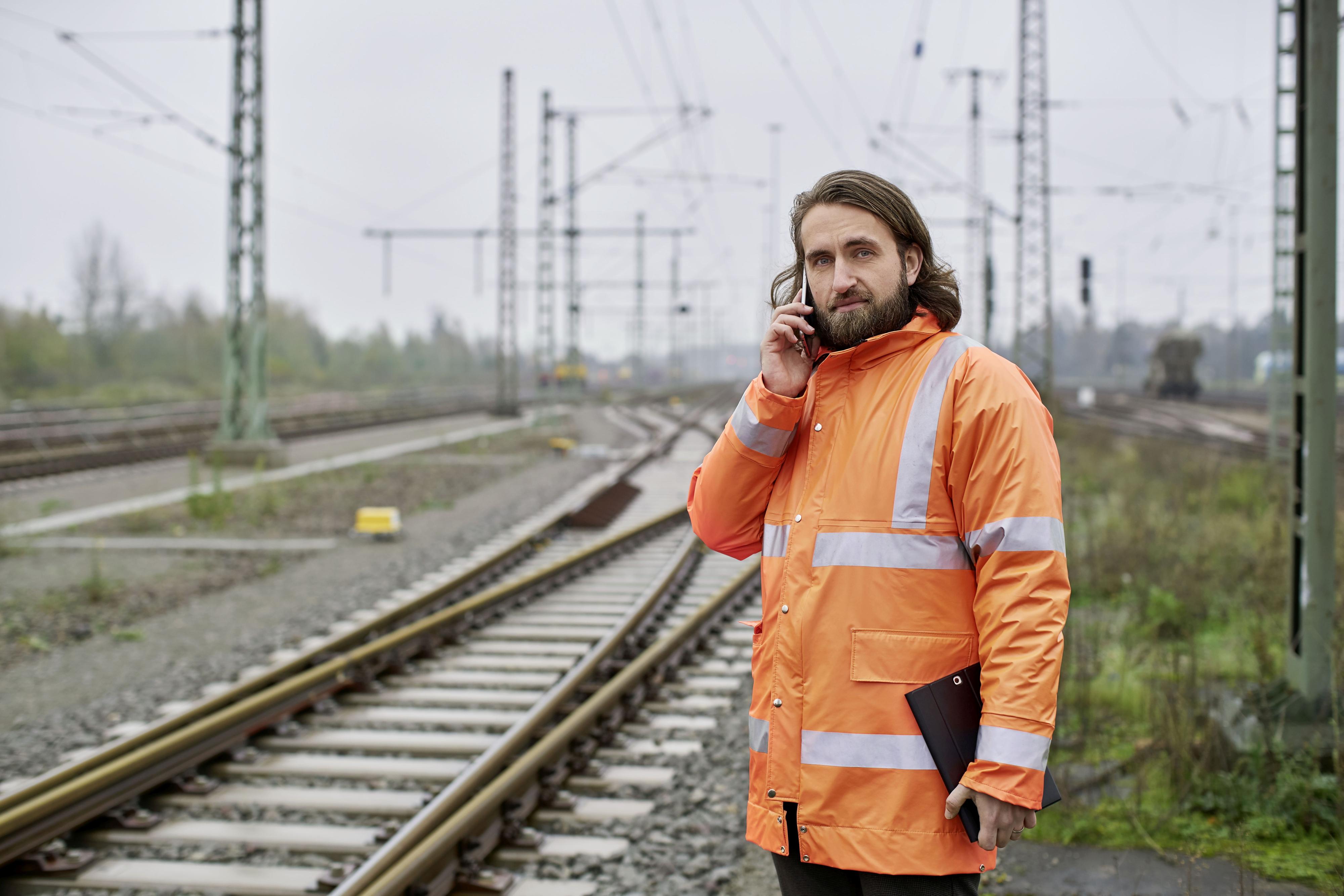 Elektroingenieur Samuel arbeitet bei der Deutschen Bahn. Er steht mit Sicherheitsweste am Gleis und telefoniert.