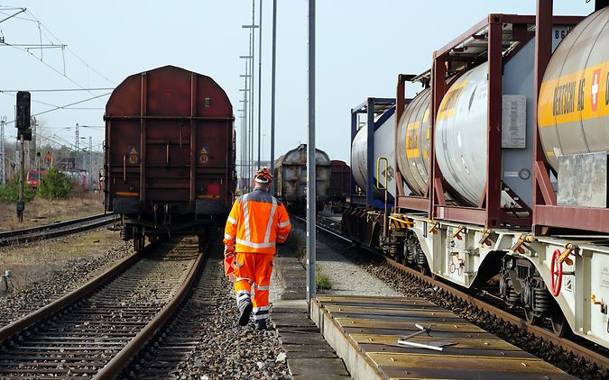 Ein Lokrangierführer in Arbeitskleidung auf den Gleisen von einem Rangierbahnhof vor haltenden Güterzügen